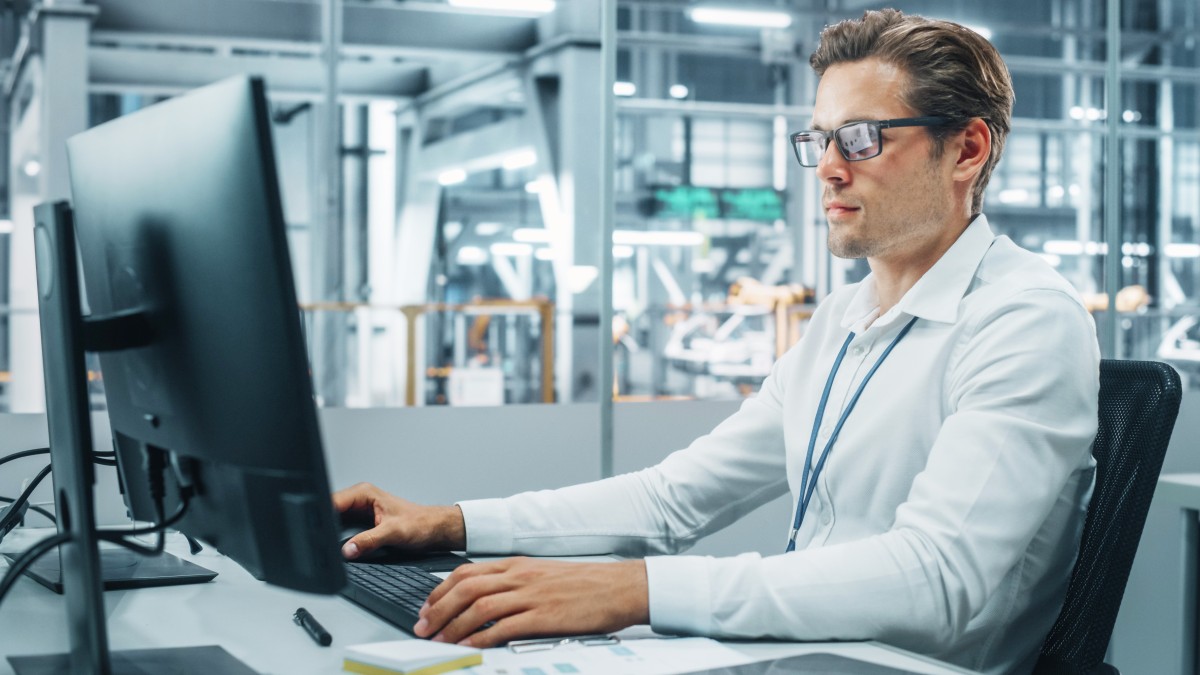 Geprüfter Industriefachwirt führt Audit am Laptop in Produktionshalle durch