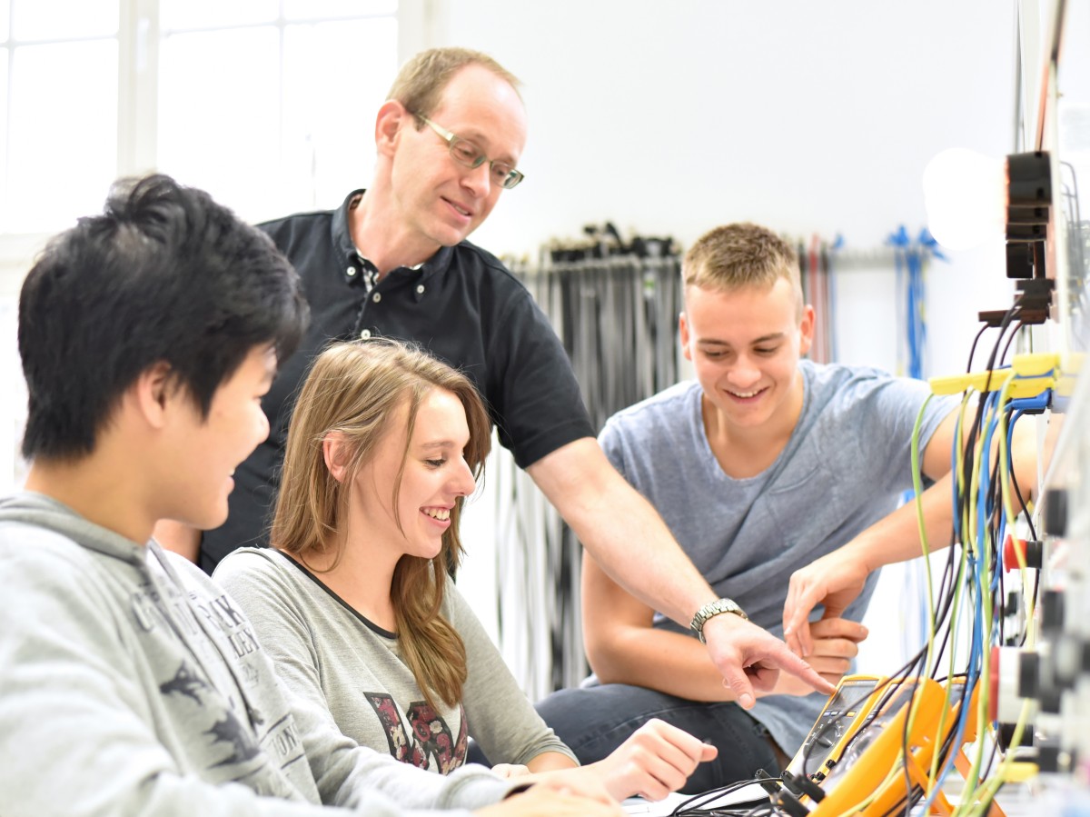 Ausbildungsberufe in der Elektrotechnik und Elektroindustrie Auszubildende und Ausbilder sitzen vor Schaltungen