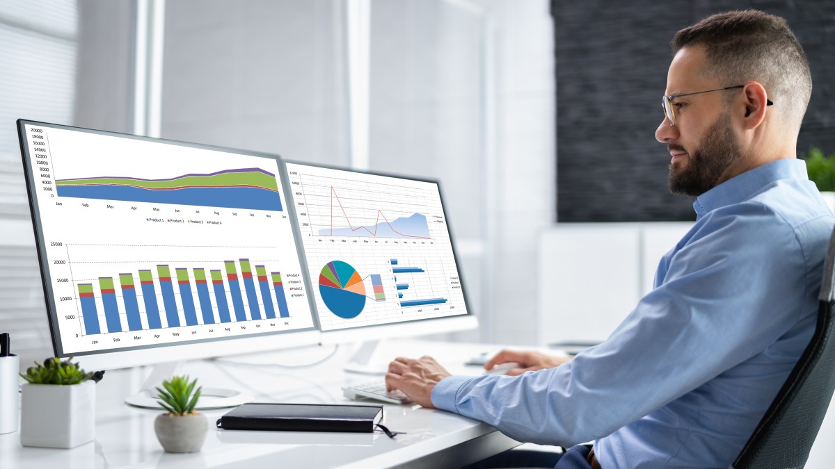 Fachwirt im IT-Commerce sitzt vor Monitoren und analysiert Online-Verkaufszahlen