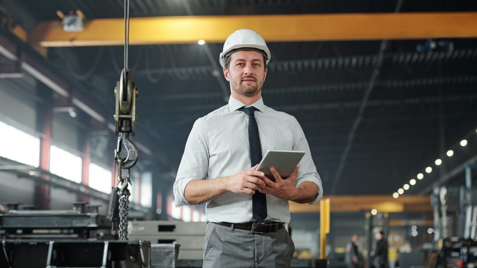 Geprüfter Industriemeister Metall plant Arbeitsabläufe digital mit Tablet in der Produktionshalle